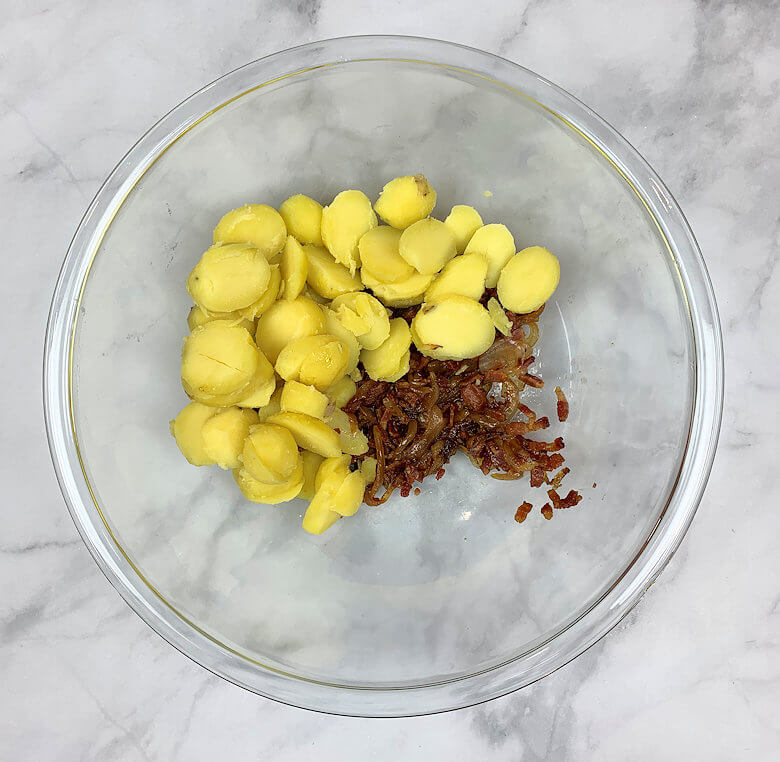 Glass bowl with potato slices, bacon and onion