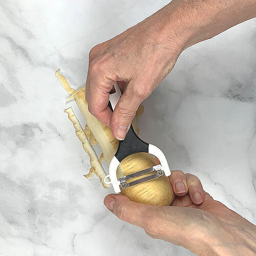 Two hands peeling parsnip with vegetable peeler